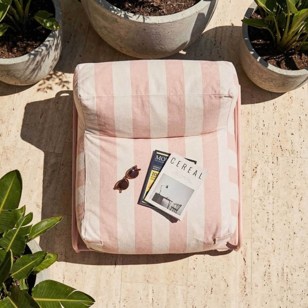 Gestreifter rosa und weißer Outdoor-Sitzsack auf einer hellen Terrasse mit Beton-Pflanzkübeln und Natursteinboden.