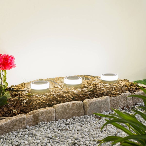 Drei runde Solar-Gartenleuchten beleuchten ein Beet mit Rindenmulch, eingefasst von Randsteinen und Kieselsteinen im Außenbereich.