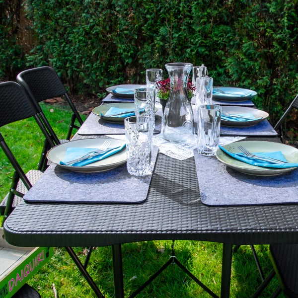 Gedeckter Gartentisch mit Geschirr, Gläsern und Dekoration für ein Essen im Freien.