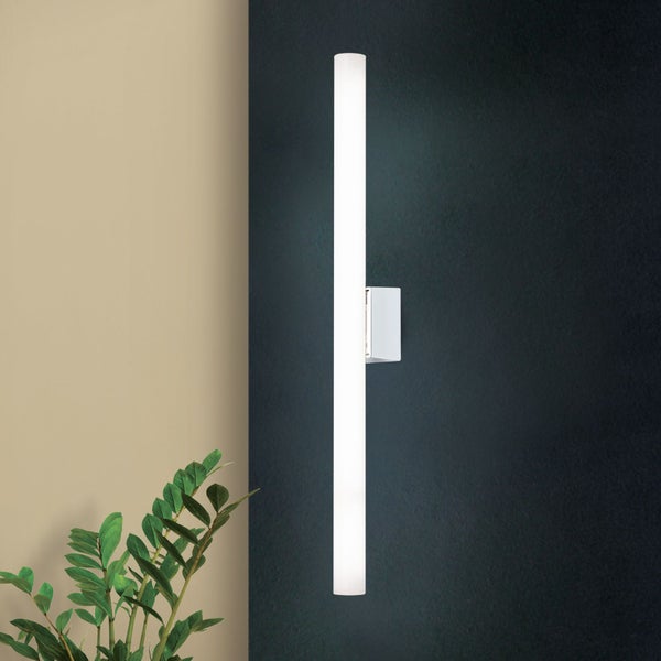 Moderne LED Wandleuchte in zylindrischer Stabform montiert an einer Wand neben einer Grünpflanze