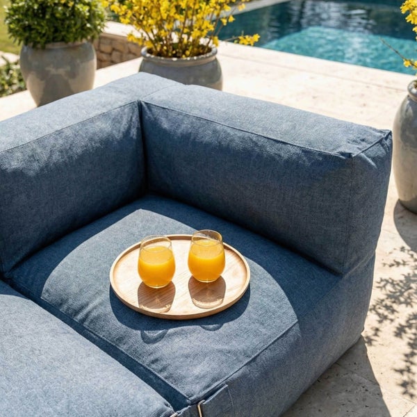 Blaues Outdoor-Lounge-Sofa aus strukturiertem Stoff auf einer Terrasse am Pool mit Holztablett und zwei Gläsern Saft.