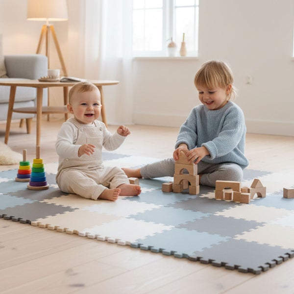 Zwei Kinder spielen auf einer Puzzlematte aus Schaumstoff mit Holzbausteinen und einem Stapelturm im hellen Wohnzimmer.