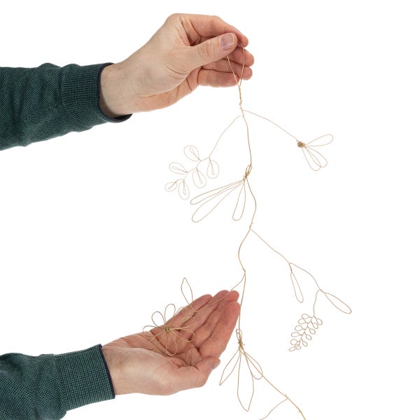 Goldfarbene Girlande aus Draht mit dekorativen Blüten- und Blattmotiven, gehalten von Händen.