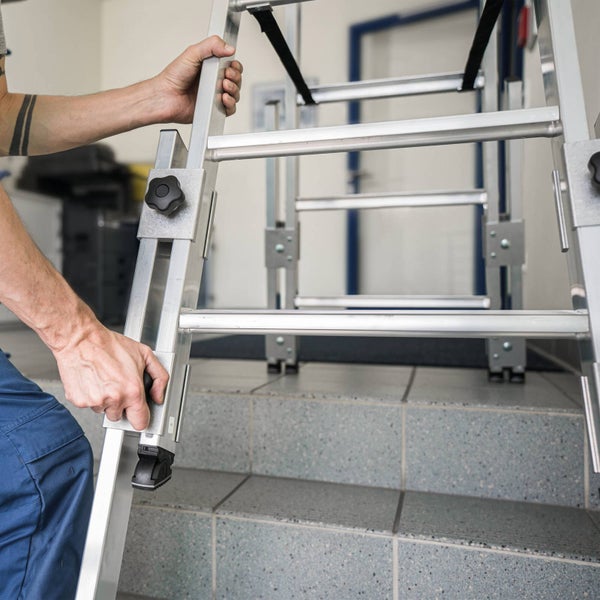 Eine Person stellt die höhenverstellbaren Beine einer Aluminiumleiter auf einer Treppe ein.