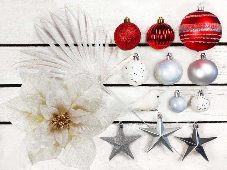 Weihnachtsdekoration Set bestehend aus Weihnachtskugeln, künstlicher Poinsettie, Palmenblatt und Sternen auf hellem Holzuntergrund.