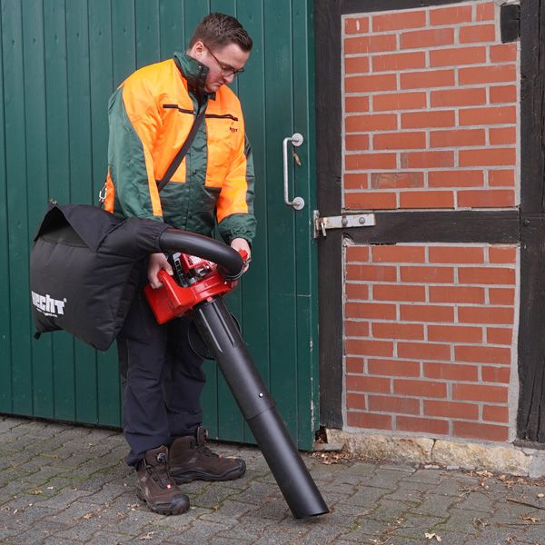 Mann mit Laubbläser vor einer grünen Tür und einer Backsteinmauer