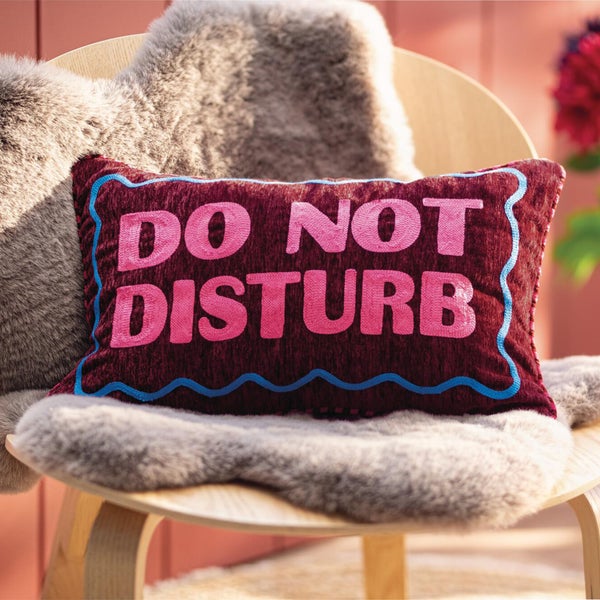 Rechteckiges Kissen mit Aufschrift Do Not Disturb auf einem Stuhl mit Kunstfellauflage