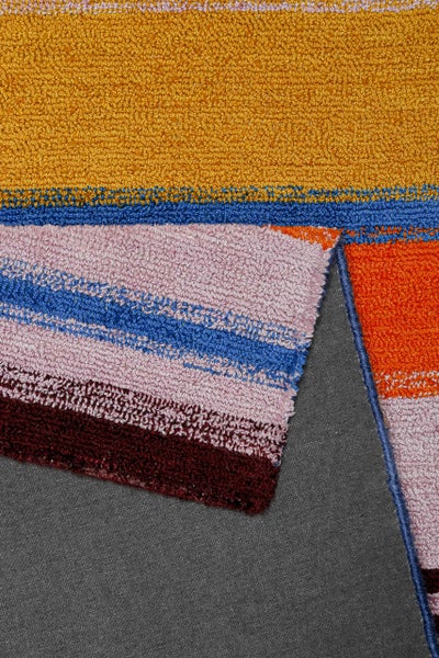 Nahaufnahme eines bunt gestreiften Teppichs mit Schlingenflor-Struktur in Gelb, Blau, Rosa, Orange und Dunkelrot.
