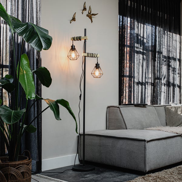 Stehlampe mit zwei Leuchten im Wohnzimmer neben Pflanze und Sofa.