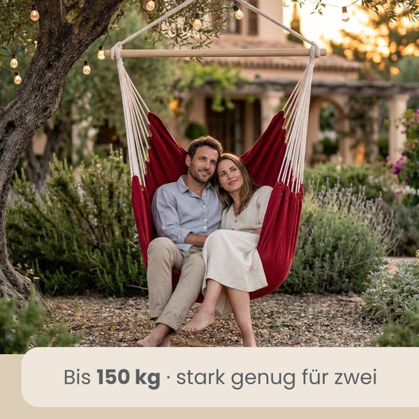 Ein Paar sitzt in einem roten Hängesessel aus Stoff im Garten. Belastbarkeit bis zu 150 Kilogramm.