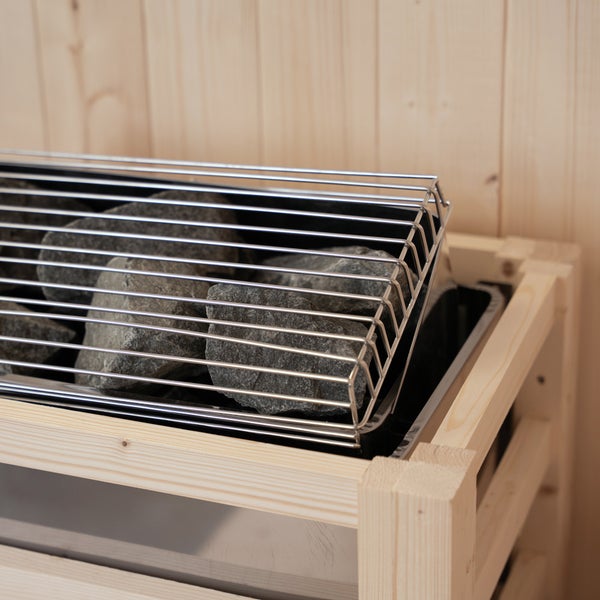 Saunaofen mit Lavasteinen in einem hölzernen Schutzgitter vor einer Wand aus hellen Holzpaneelen.