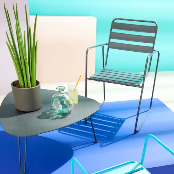 Moderner Gartenstuhl aus Metall mit Armlehnen und passender dreieckiger Gartentisch mit einer Pflanze im Topf.