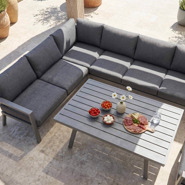 Modernes Garten-Lounge-Set aus Metall mit großer Eckcouch und Polstern auf einer hellen Terrasse mit rechteckigem Lamellentisch.