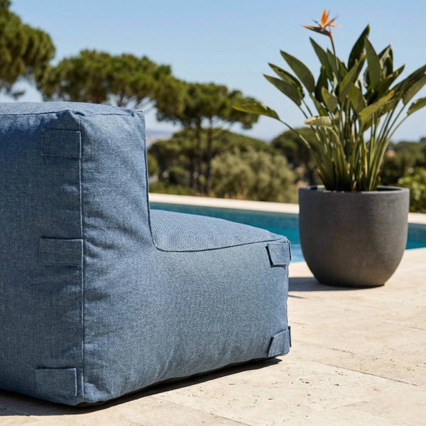 Blauer Outdoor-Sitzsack auf einer Terrasse neben einem Pool, im Hintergrund Bäume und eine Pflanze im Topf.