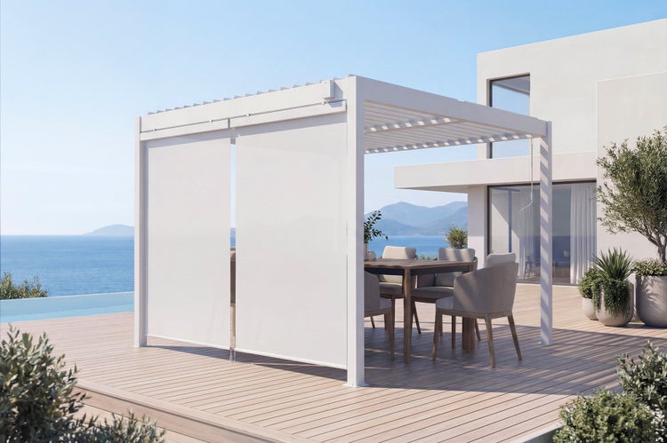 Moderne Bioklimatische Pergola mit Lamellendach und Seitenmarkisen auf einer Holzterrasse vor einem Wohnhaus mit Blick auf das Meer.