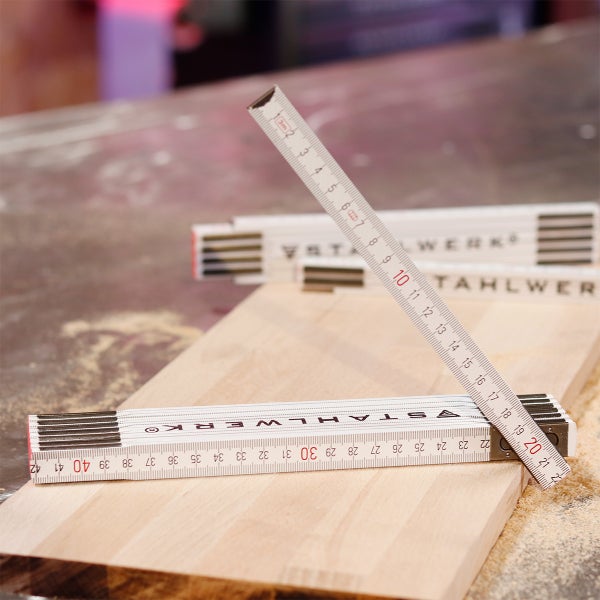 Gliedermaßstab aus Holz auf einem Holzbrett in einer Werkstatt.