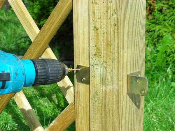 Eine Bohrmaschine schraubt eine Metallhalterung an einen Holzzaun