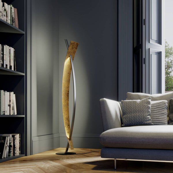 Moderne, skulpturale Stehleuchte in Gold- und Silberoptik in einem Wohnzimmer mit Parkettboden, Sofa und Bücherregal.