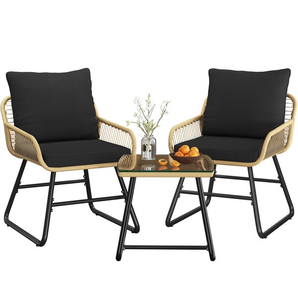 Gartenset mit zwei Rattansesseln, schwarzen Kissen und einem Glasbeistelltisch.
