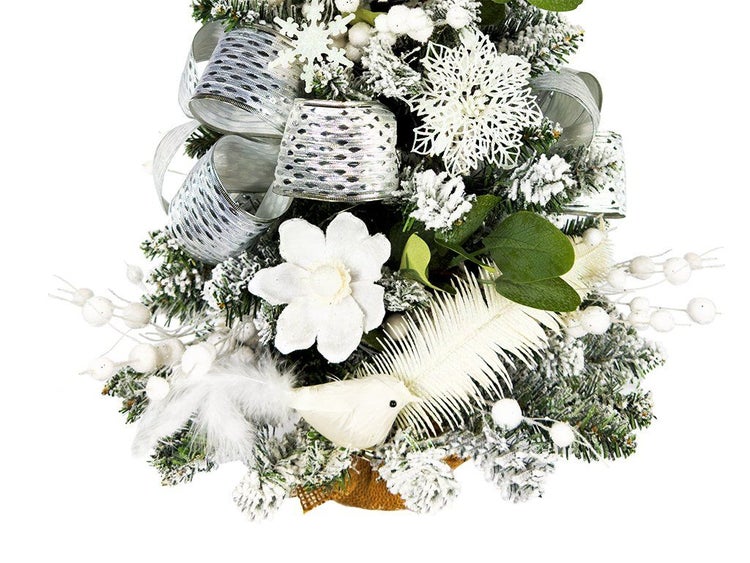 Künstlicher Weihnachtsbaum mit Schnee, Schleifen, Blumen, Federvogel und Beeren als weihnachtliche Dekoration.