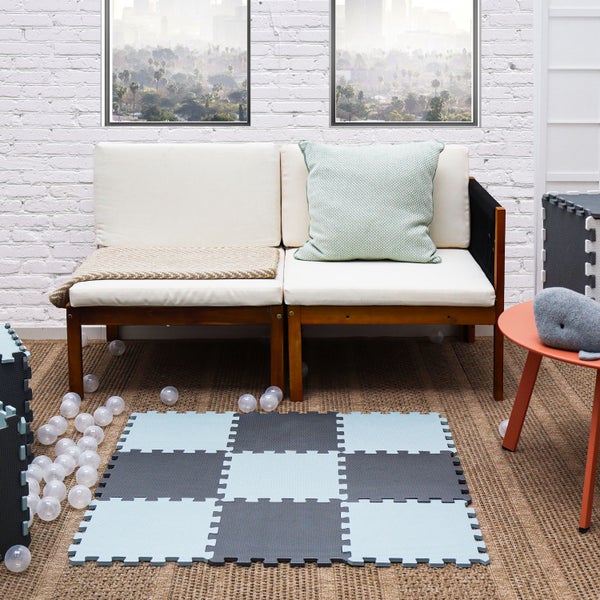 Spielmatte als Puzzlematte aus Schaumstoff in Schachbrettoptik vor einem Holzsofa mit Kissen in einem modern eingerichteten Wohnbereich.