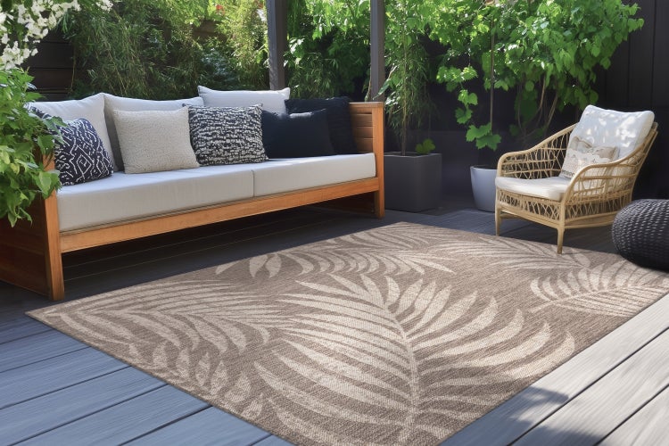 Outdoor Teppich mit Blättermotiv auf einer Terrasse mit Lounge Sofa und Korbsessel.
