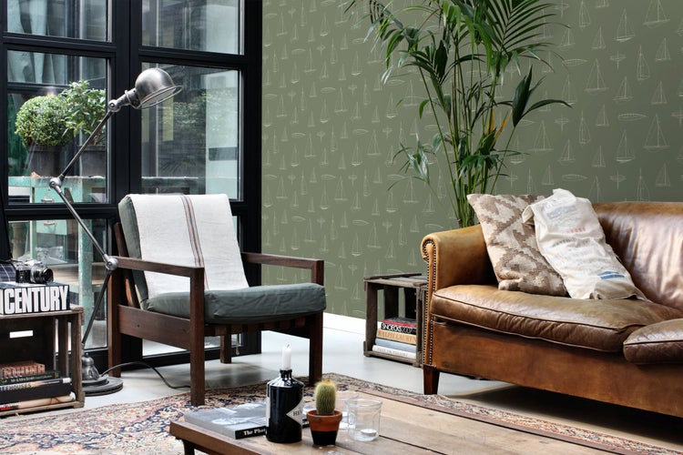 Wohnzimmer mit grüner Tapete mit Segelschiff-Muster, Ledersofa, Holzarmsessel, Stehlampe und einer großen Zimmerpflanze.