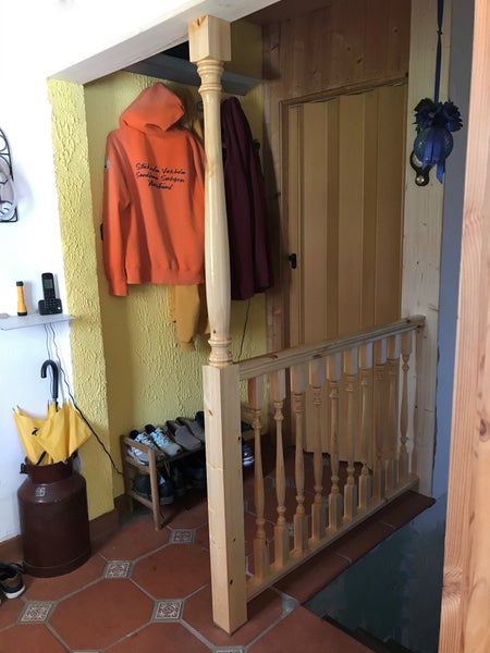 Treppengeländer aus Holz mit gedrechselten Geländerstäben und Pfosten im Eingangsbereich mit Fliesenboden.