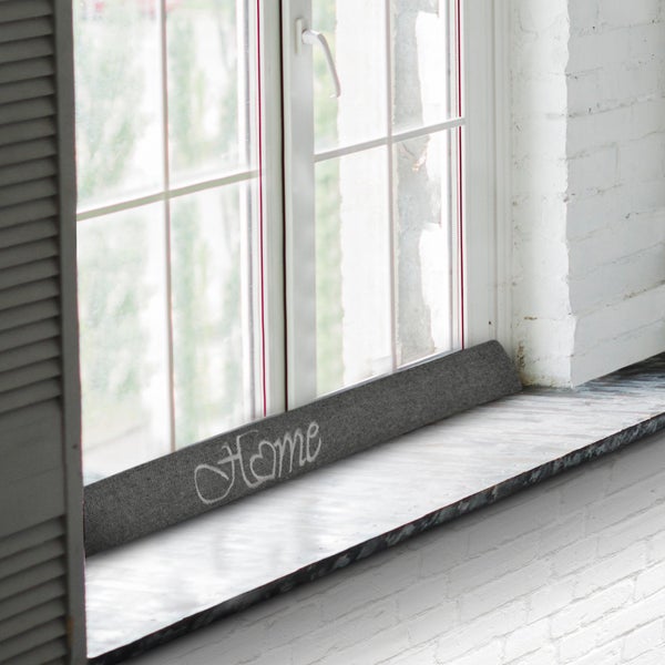 Zugluftstopper mit dem Schriftzug Zuhause vor einem Fenster