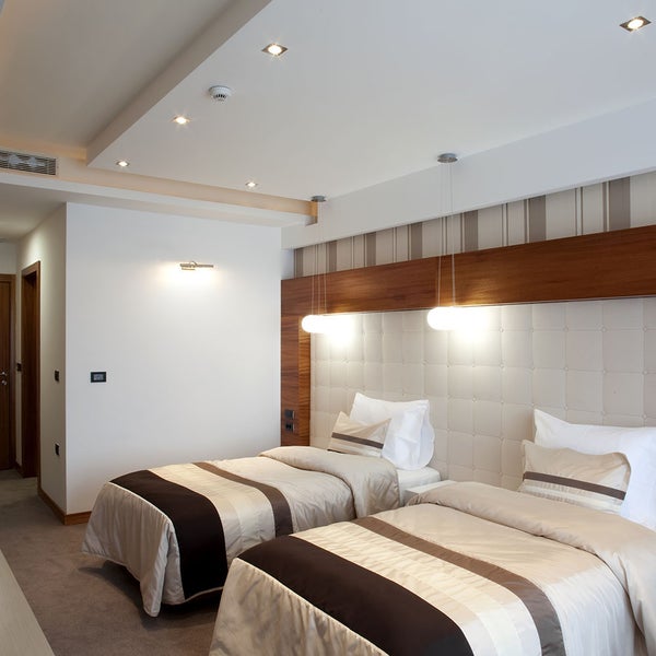 Modernes Schlafzimmer mit zwei Einzelbetten, gepolstertem Kopfteil, abgehängter Decke mit Einbaustrahlern und zwei Pendelleuchten.