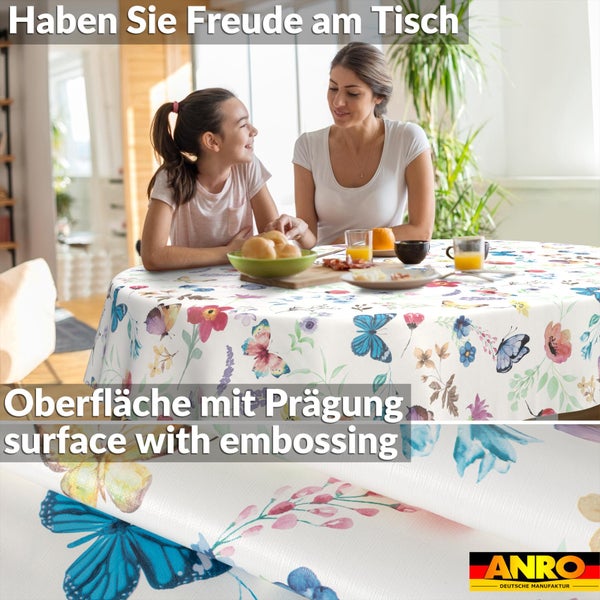 Runde Tischdecke mit Blumen- und Schmetterlingsmuster in hellem Esszimmer mit Mutter und Kind. Detail der Prägung. ANRO Logo.