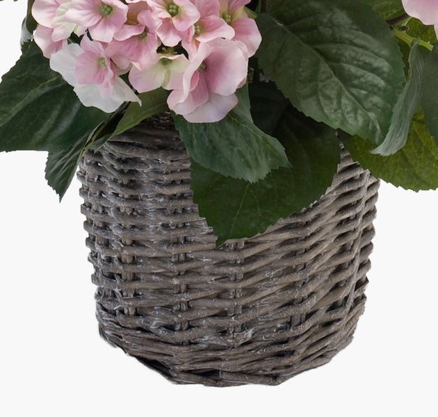Künstliche rosa Hortensie mit grünen Blättern in einem grauen geflochtenen Korb.
