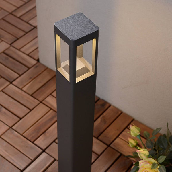 Moderne, quadratische Wegeleuchte aus Metall mit warmweißem Licht auf einer Terrasse mit Holzbodenplatten.