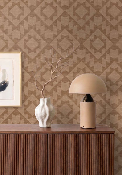 Wohnraum mit Vliestapete mit geometrischem Muster, Holzanrichte, Tischleuchte und Dekovase an einer Wand