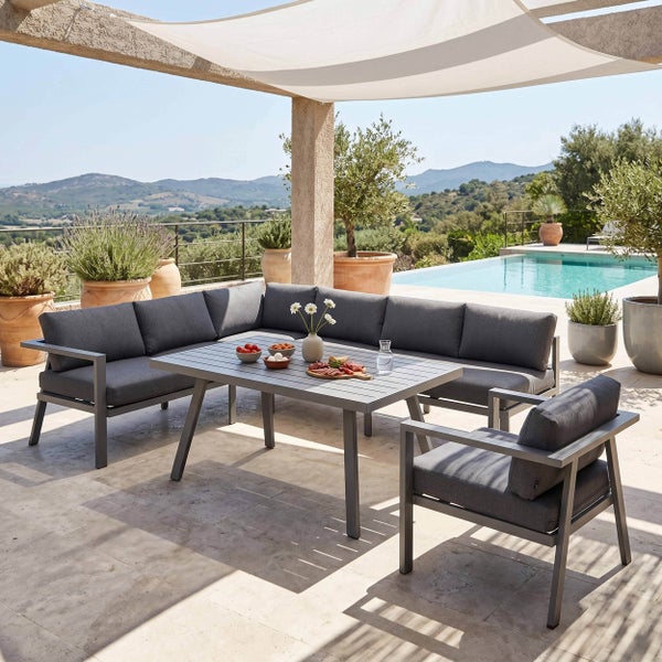 Moderne Garten-Lounge-Gruppe aus Metall mit grauem Ecksofa, Sessel und Tisch auf einer hellen Terrasse mit Pool und Landschaftsblick.