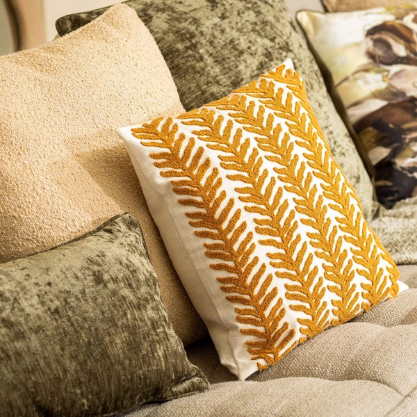 Mehrere dekorative Kissen auf einem Sofa, darunter ein weißes Kissen mit Blattmuster