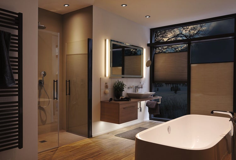 Modernes Badezimmer mit freistehender Badewanne, begehbarer Glasdusche, Holz-Waschtisch, beleuchtetem Spiegel und schwarzem Handtuchheizkörper.