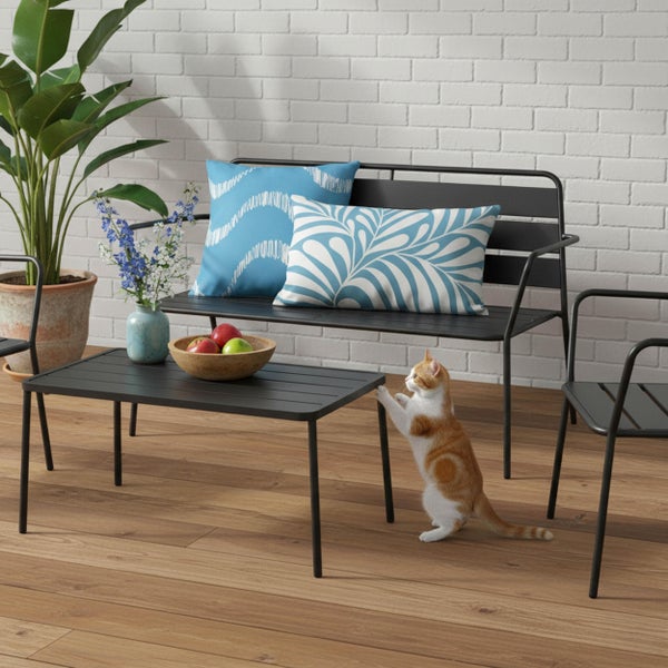 Modernes Gartenmöbel-Set aus schwarzem Metall mit Bank, Couchtisch und Stuhl auf einer Holzterrasse vor einer weißen Ziegelwand.