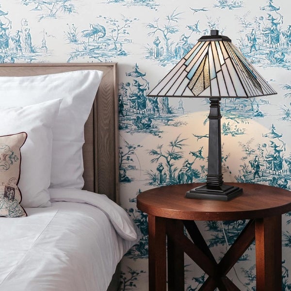 Dekorative Tiffany Lampe auf einem Nachttisch neben einem Bett vor einer gemusterten Tapete.