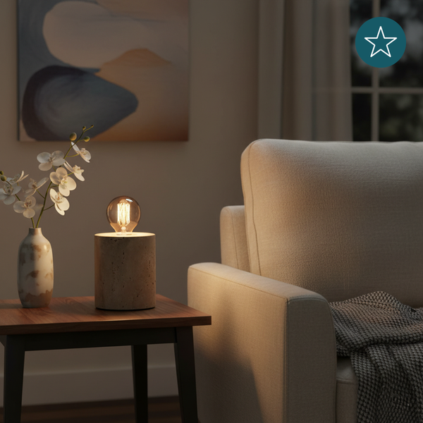Dekorative Tischlampe mit Betonfuß und Glühbirne auf einem Beistelltisch neben einem Sessel.