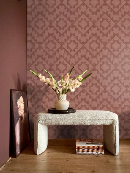 Wohnraum mit Vliestapete mit geometrischem Muster, Sitzbank mit Boucle Bezug, Blumen in Vase und einem gerahmten Bild auf dem Holzboden.