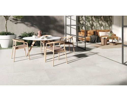 Moderne Terrassenfliesen in Steinoptik verlegt auf einem hellen Außenbereich mit Sitzgruppe und Glasfront im Hintergrund.