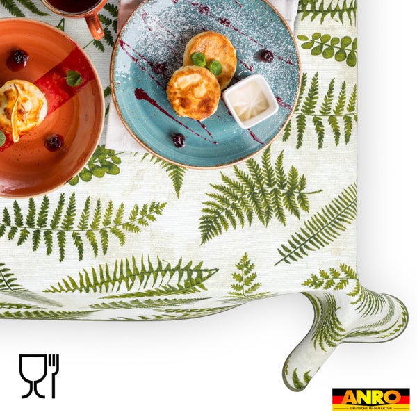 Abwischbare Tischdecke mit Farnblattmuster, dargestellt in einer Essensszene mit Tellern. Lebensmittelecht Symbol. ANRO Logo.