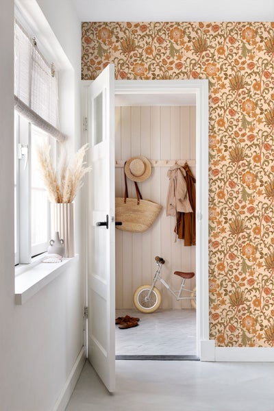 Helles Zimmer mit gemusterter Blumentapete, weißer Tür, Fensterbank mit Pampasgras und Blick in einen Flur mit Holzwandpaneelen.