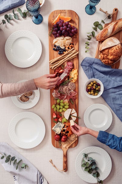 Dekorativer Tisch mit Geschirr, Brot, Oliven, Wurst, Käse, Obst und Kräutern.