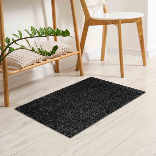 Dunkelgrauer rechteckiger Hochflor-Teppich auf hellem Holzboden in einem modernen Raum mit Holzregal und Pflanze.