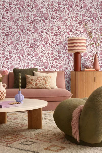 Wohnzimmer mit florale Tapete im Vintage Design, gemütliches Sofa mit verschiedenen Dekokissen, runder Couchtisch und moderne Beleuchtung.