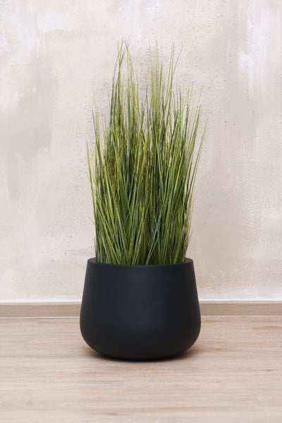 Künstliche Graspflanze in einem runden, matt-schwarzen Blumentopf.