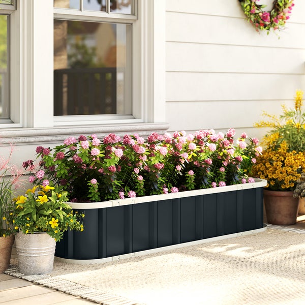 Hochbeet aus Metall in Anthrazit mit weißem Rand, bepflanzt mit rosa Blumen auf einer hellen Terrasse vor einer Hauswand.