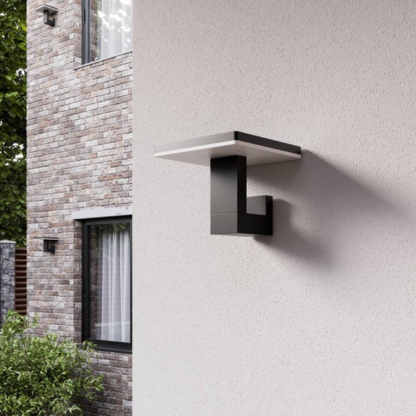 Moderne LED-Außenwandleuchte in Anthrazit an einer hellgrau verputzten Hausfassade neben einer Klinkerwand mit Fenstern.